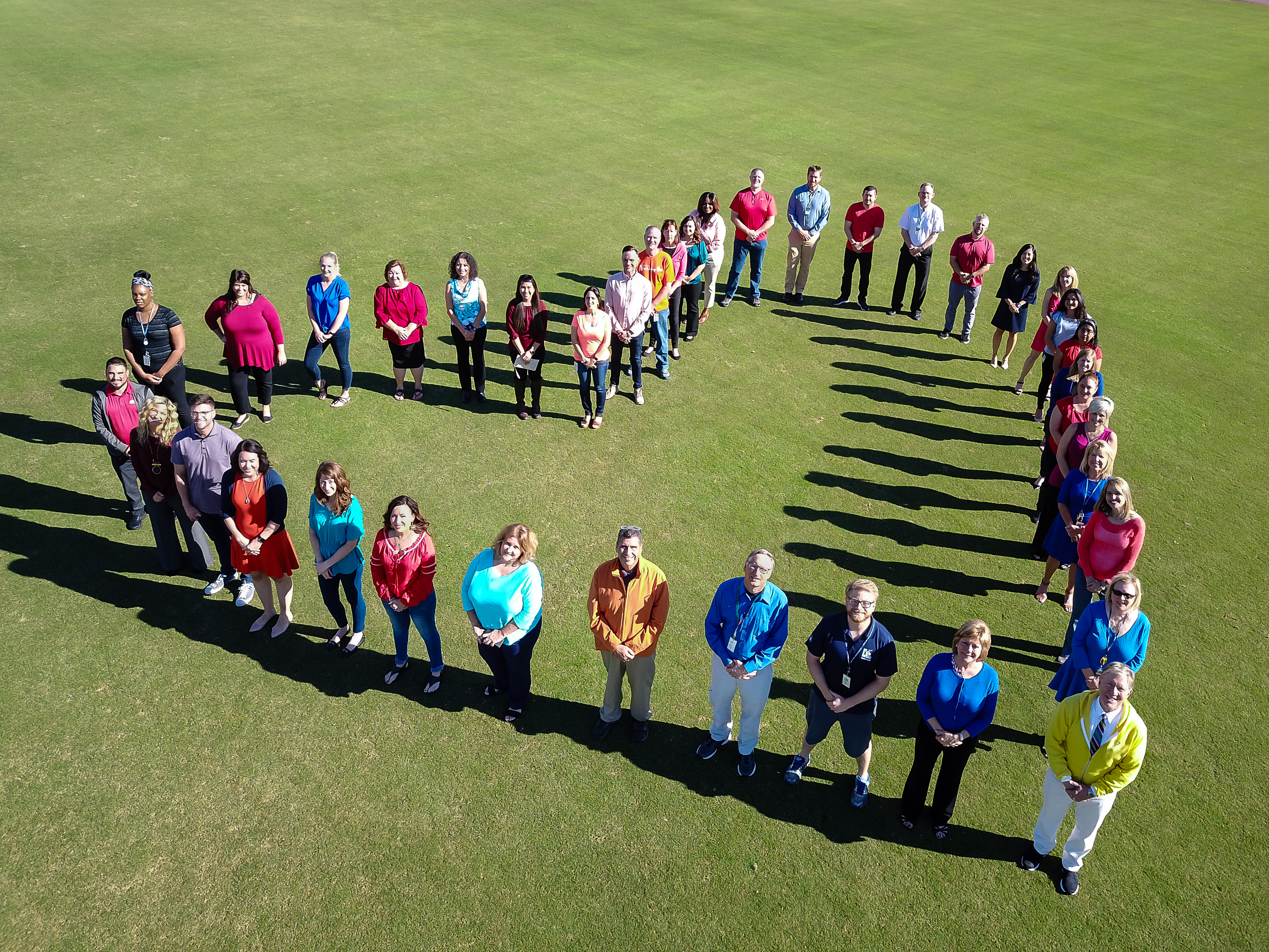 A group of people in a field, arranged in a heart pattern